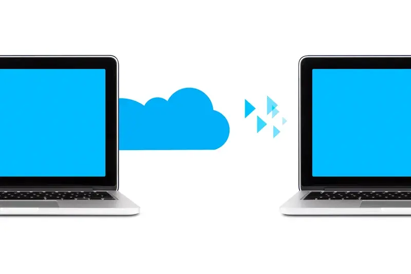 Two laptops sit side by side, transferring data through the cloud