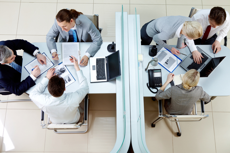 Two groups of people gather around two cubicles to collaborate