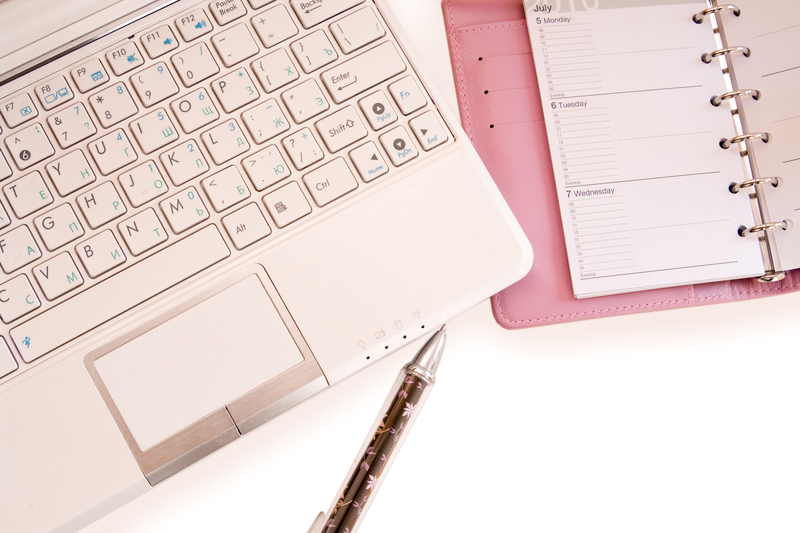 A laptop keyboard, pen, and notebook planner sit on a desk