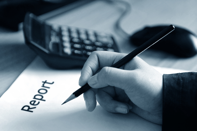 A paper titled Report is on a desk in front of a hand holding a pencil