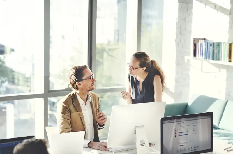 Two colleagues have a discussion over a computer.