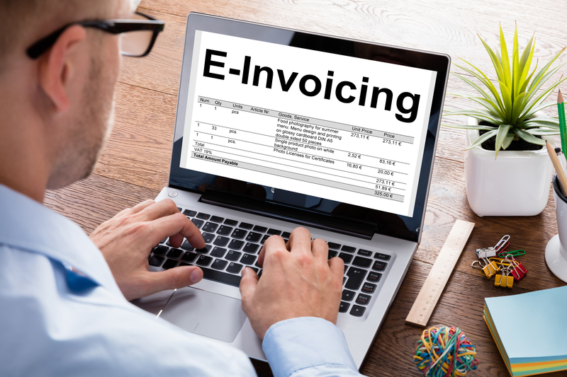 Stock photo of a man with glasses looking down at a laptop with 'e-invoicing' on the screen.